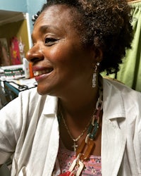 a woman in a white shirt smiling in front of a sewing machine